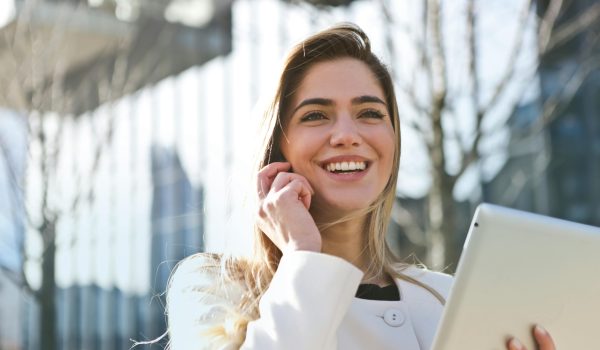 Confident businesswoman using her tablet and phone, smiling outdoors in sunlight.